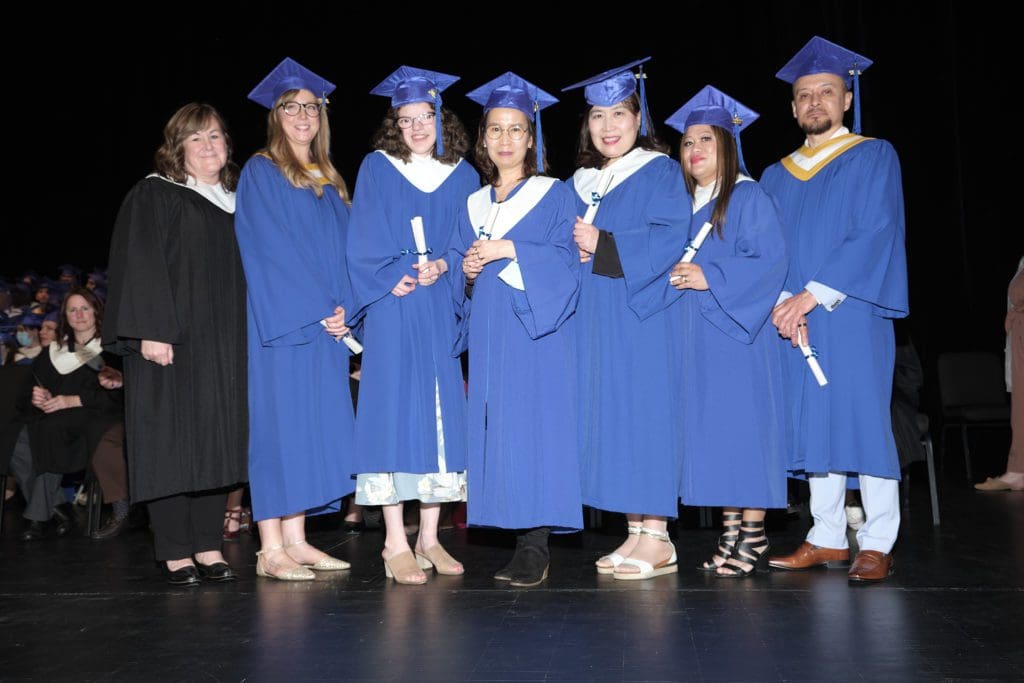 Natasha and her classmates wearing royal blue graduation gowns take a photo during their ceremony